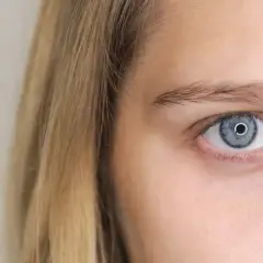 Zbliżenie na niebieskie oko z refleksami, obok blond włosy. Jedno oko mniejsze, ale równie hipnotyzujące.