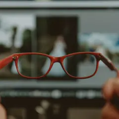 Czerwone okulary przed ekranem komputera, na którym widać rozmazane zdjęcia. Poprawiają widzenie obuoczne.