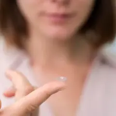 Kobieta trzyma soczewkę kontaktową na palcu. Czy to za mocne soczewki, objawy mogą być niepokojące.