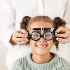Mała dziewczynka uśmiecha się, gdy optometrysta sprawdza jej wzrok za pomocą okularów próbnych, diagnozując astygmatyzm u niemowlaka.