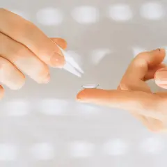 Dłoń z soczewką kontaktową na palcu, obok pęseta. Może to być początek dyskomfortu w jednym oku.