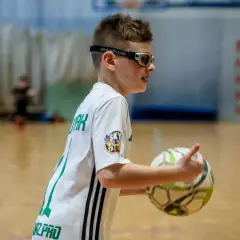 Chłopiec w okularach korekcyjnych do gry w piłkę nożną trzyma piłkę, gotowy do akcji na boisku.