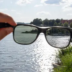 Widok jeziora przez okulary z polaryzacją. Słońce odbija się od wody, tworząc błyszczące refleksy.