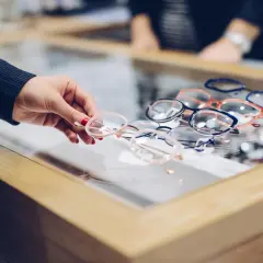 Ręka wybiera okulary z wystawy. Czy optyk zrobi okulary bez recepty? Wiele modeli czeka na klientów.