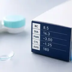 Pudełko z soczewkami kontaktowymi, na którym widnieje parametr PWR -3.00. Obok leży pojedyncza soczewka i pojemniczek.