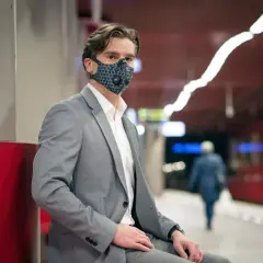 Mężczyzna w garniturze i masce na twarzy, czekający na peronie. Parowanie okularów to problem, ale nie dla niego.