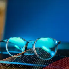 Okulary przeciw niebieskiemu światłu leżą na klawiaturze laptopa, chroniąc oczy przed ekranem.
