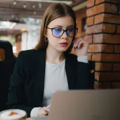 Kobieta w okularach z niebieskimi soczewkami pracuje przy laptopie. Czy okulary poprawiają wzrok? To pytanie zadaje sobie wiele osób.