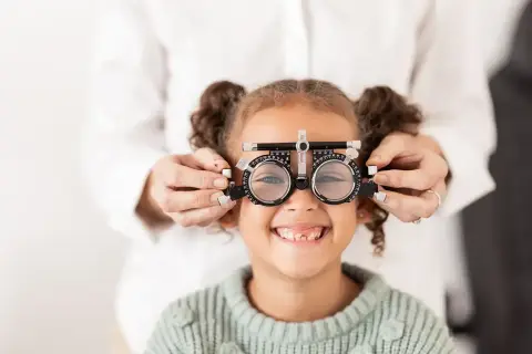 Mała dziewczynka uśmiecha się, gdy optometrysta sprawdza jej wzrok za pomocą okularów próbnych, diagnozując astygmatyzm u niemowlaka.