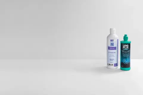 Dwie butelki płynu do soczewek: jedna z napisem "EYE SEE SALINE SOLUTION", druga "LENS PLUS OcuPure".