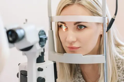 Kobieta z blond włosami poddawana badaniu wzroku. Okular na jedno oko jest częścią urządzenia diagnostycznego.