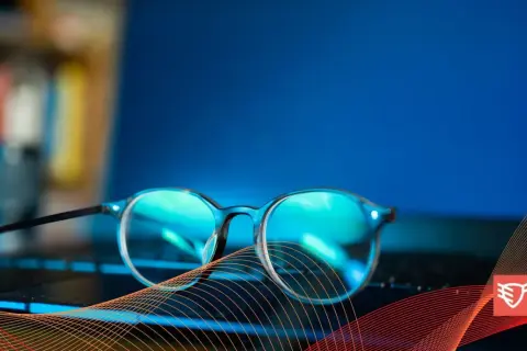 Okulary przeciw niebieskiemu światłu leżą na klawiaturze laptopa, chroniąc oczy przed ekranem.
