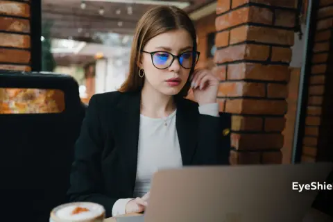 Kobieta w okularach z niebieskimi soczewkami pracuje przy laptopie. Czy okulary poprawiają wzrok? To pytanie zadaje sobie wiele osób.