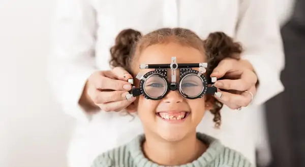 Mała dziewczynka uśmiecha się, gdy optometrysta sprawdza jej wzrok za pomocą okularów próbnych, diagnozując astygmatyzm u niemowlaka.