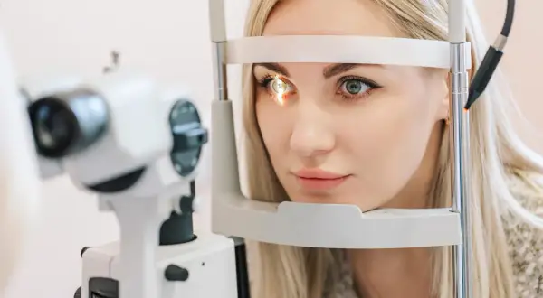 Kobieta z blond włosami poddawana badaniu wzroku. Okular na jedno oko jest częścią urządzenia diagnostycznego.