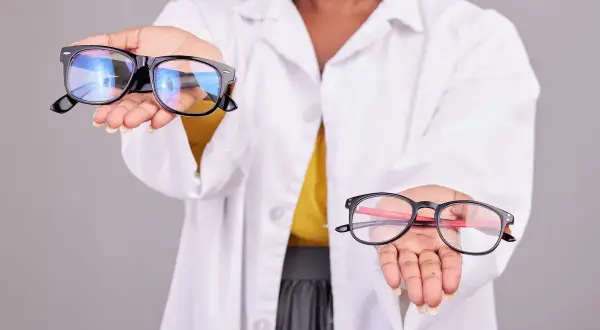 Osoba w białym kitlu prezentuje dwie pary okularów. Czy okulary z apteki szkodzą? Zastanówmy się nad tym.