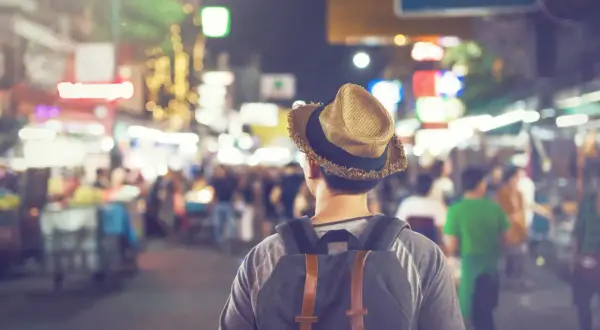 Mężczyzna w kapeluszu i z plecakiem idzie nocą przez tętniący życiem bazar. To jego widzenie w ciemności, pełne kolorowych świateł i ludzi.
