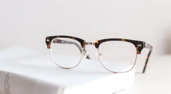 Okulary z oprawkami w stylu retro, idealne do korygowania wady wzroku +2. Leżą na białej książce.