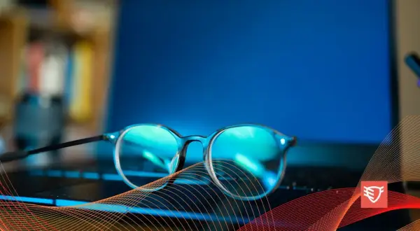 Okulary przeciw niebieskiemu światłu leżą na klawiaturze laptopa, chroniąc oczy przed ekranem.