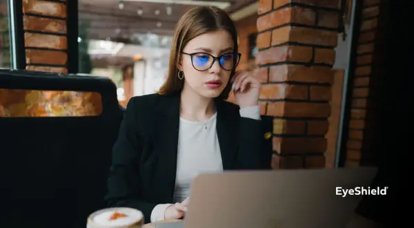 Kobieta w okularach z niebieskimi soczewkami pracuje przy laptopie. Czy okulary poprawiają wzrok? To pytanie zadaje sobie wiele osób.