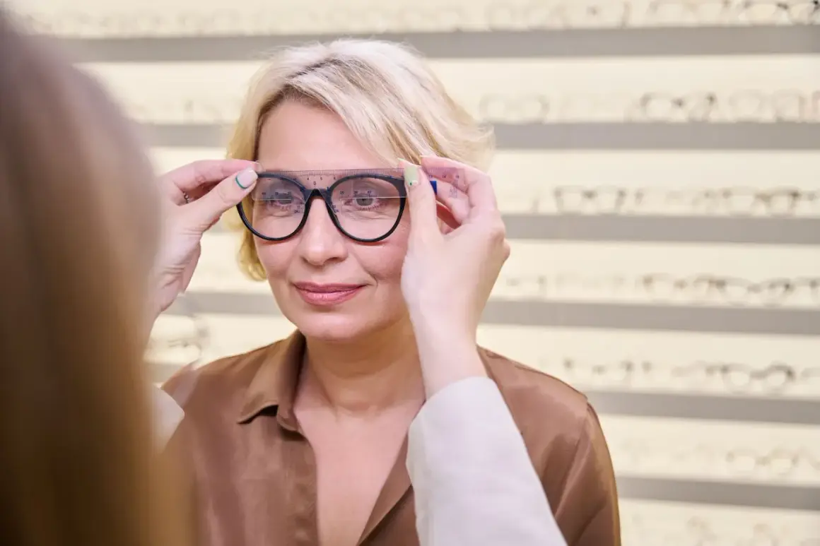 Optometrysta mierzy okulary klientce, przygotowując dokumentację do refundacji okularów dla emeryta.