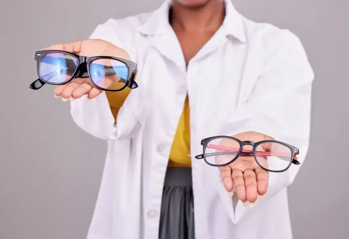 Osoba w białym kitlu prezentuje dwa modele okularów. Jedne, większe, z czarnymi oprawkami, drugie, mniejsze, z czarno-czerwonymi oprawkami. To dwuogniskowe okulary.