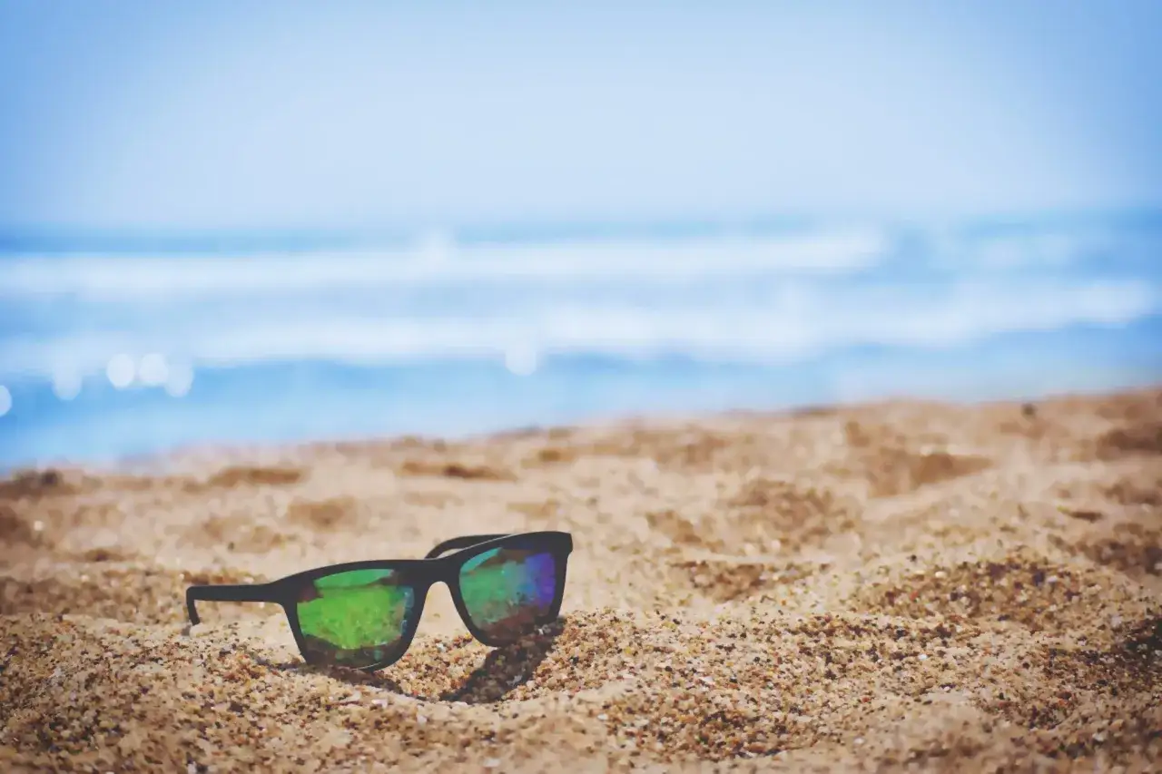 Okulary kategoria 3 leżą na piaszczystej plaży, odbijając błękitne niebo i morze. Idealne na słoneczny dzień.