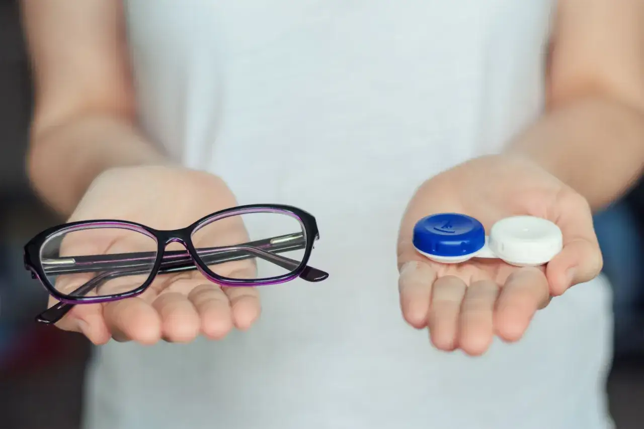 Dwie dłonie prezentują wybór: okulary i pojemnik na soczewki. Czy można nosić soczewki i okulary jednocześnie? To pytanie o korekcję wzroku.
