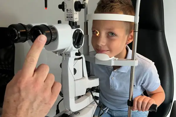 Chłopiec podczas badania wzroku u okulisty. Lekarz bada oko, a chłopiec uśmiecha się. Badanie jest ważne, by wykluczyć ewentualne krople joalis skutki uboczne.