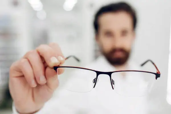 Mężczyzna z brodą trzyma okulary. Tak widzi krótkowidz bez korekcji.