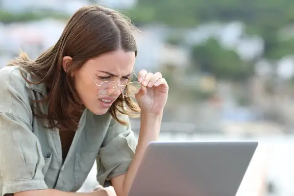 Kobieta z wadą wzroku -0.75, z trudem czyta tekst na laptopie, poprawiając okulary.