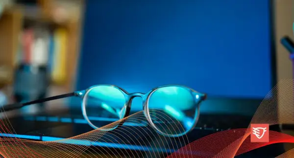 Okulary przeciw niebieskiemu światłu leżą na klawiaturze laptopa, chroniąc oczy przed ekranem.