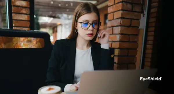 Kobieta w okularach z niebieskimi soczewkami pracuje przy laptopie. Czy okulary poprawiają wzrok? To pytanie zadaje sobie wiele osób.